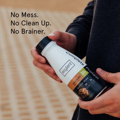 Soylent Complete Protein Shake Chocolate on desk with glass, ready-to-drink convenience.