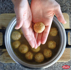 Matzo balls cooking in simmering chicken broth with steam rising.