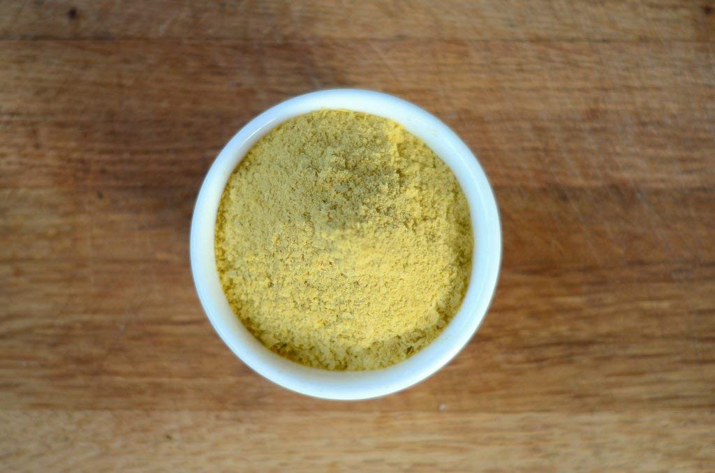 Sprinkling Anthony's Nutritional Yeast Flakes on pasta for savory flavor.
