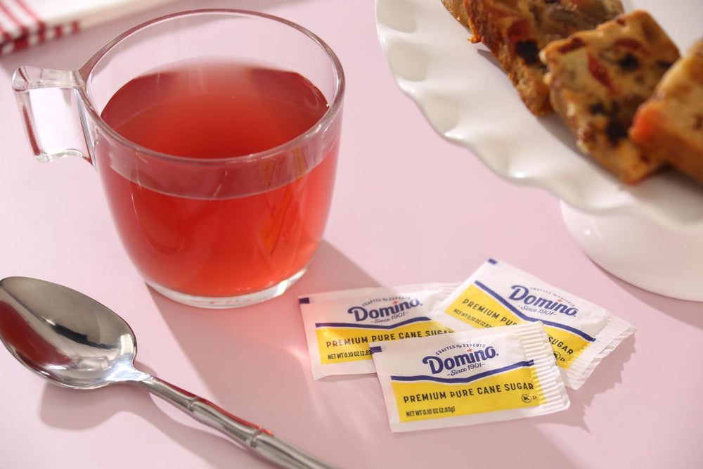 Domino sugar packets on a countertop with a coffee cup for daily use.