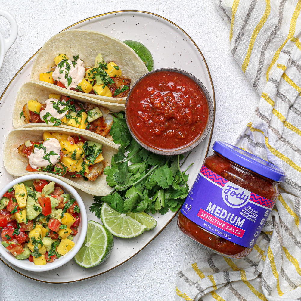 Pouring Fody salsa to top tacos for a zesty finish.