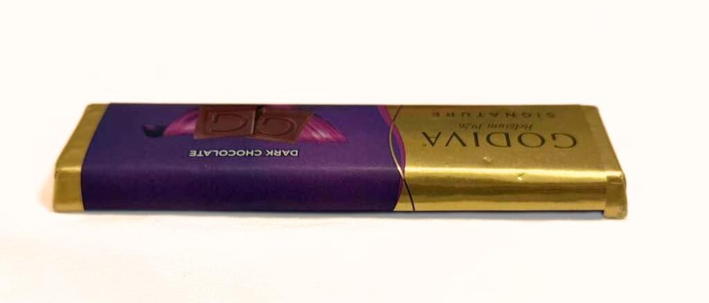 Godiva dark solid bar slice breaking, showcasing smooth interior and firm snap.