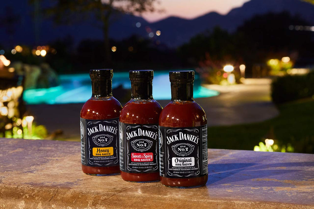 Serving bowl with Jack Daniels Barbeque Sauce Sweet and Spicy beside grilled foods.