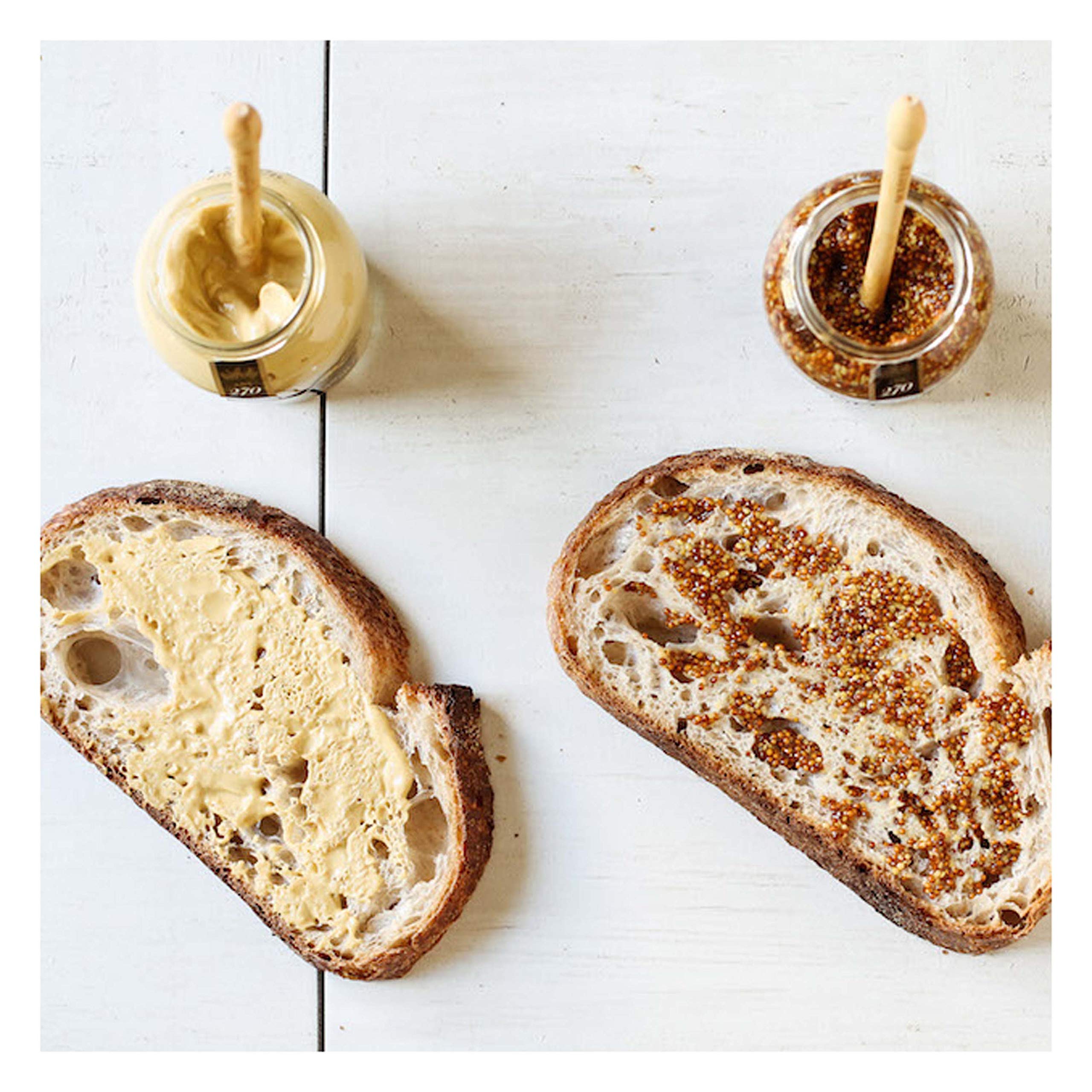 Maille mustard spread on sandwich ready to elevate flavor.