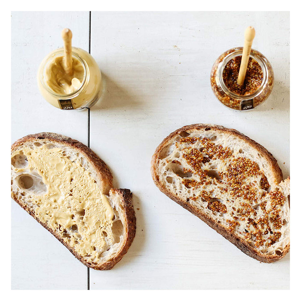 Maille mustard spread on sandwich ready to elevate flavor.