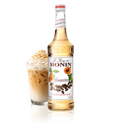 Monin Amaretto Syrup bottle on a bar setup, enhancing coffees and cocktails.