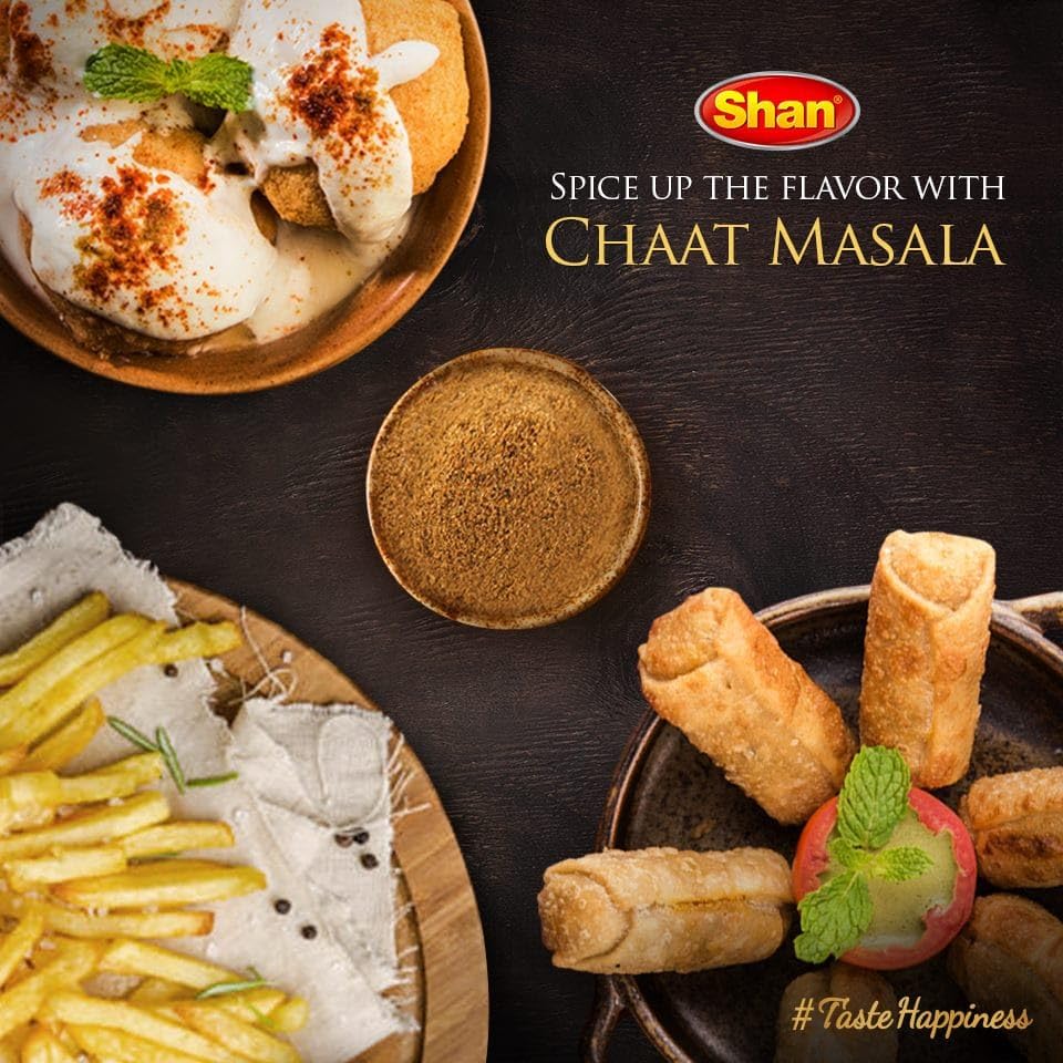 Teaspoon sprinkling Shan Masala over food for tangy flavor boost.