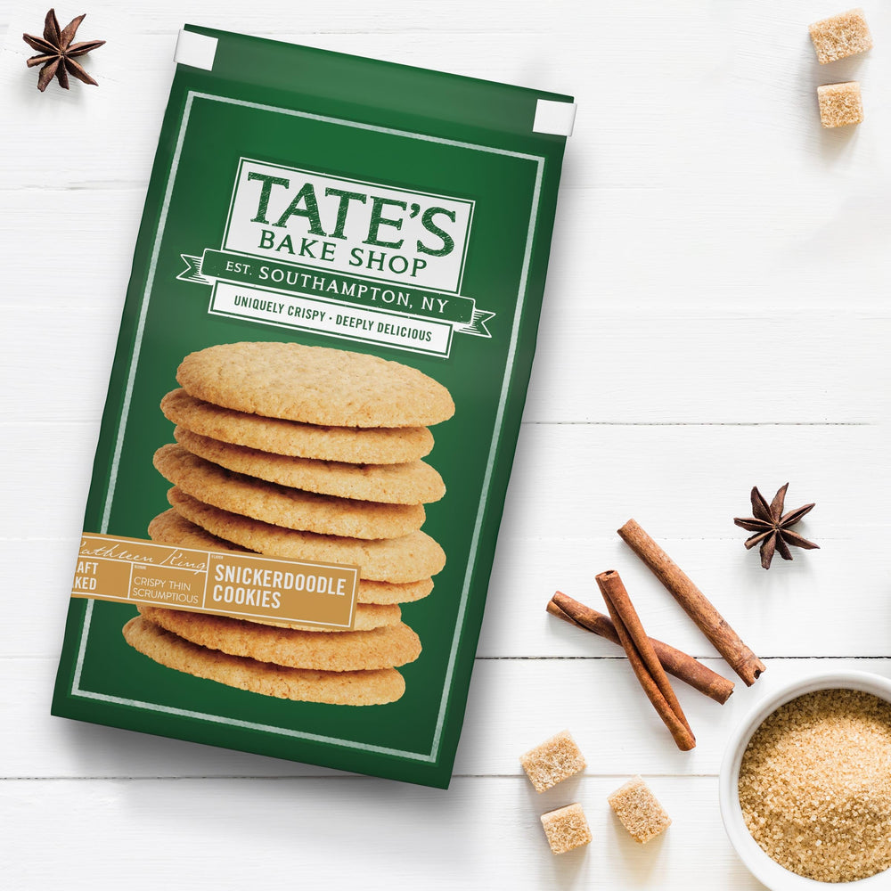 Tate's Snickerdoodle cookies beside a hot beverage in a cozy setting