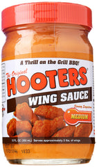 The Original Hooters Wing Sauce Medium bottle being poured over hot wings for flavor.