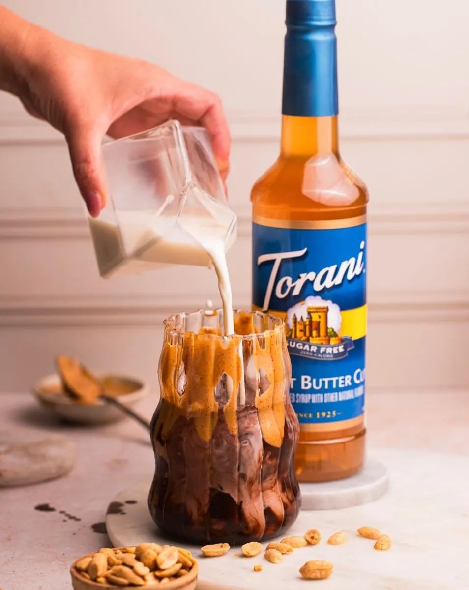Torani Sugar-Free Peanut Butter Cup bottle beside a coffee cup in a cafe setting.