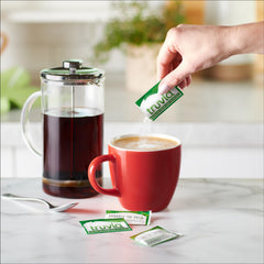 Truvia bottle-dispense pack beside coffee mug for quick sweetening.