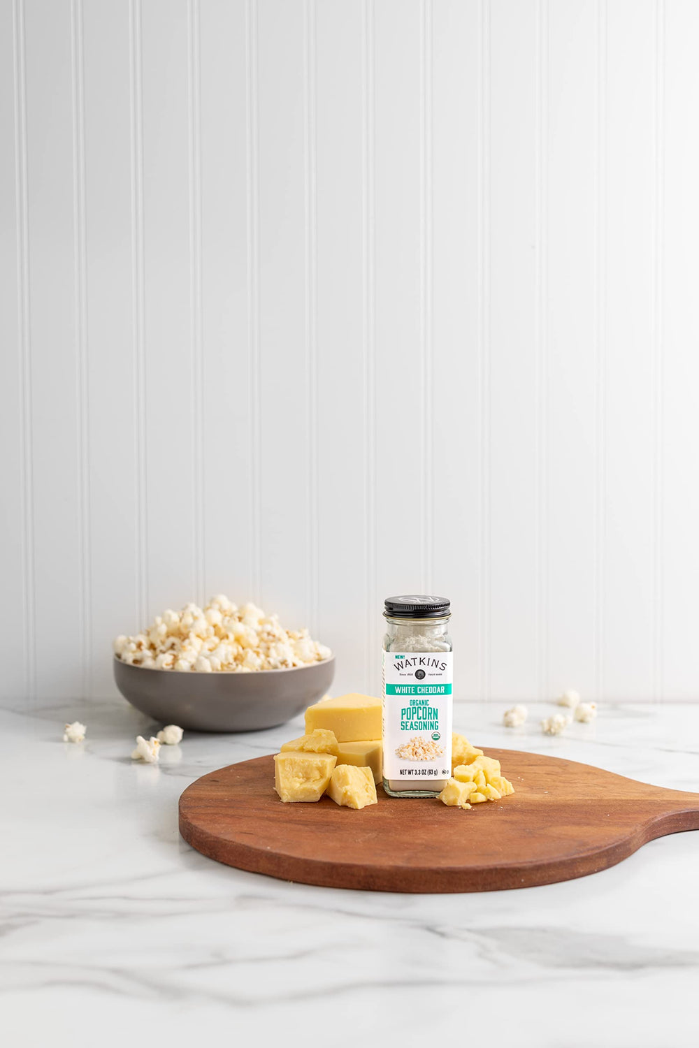 Watkins white cheddar seasoning dusted over popcorn for flavor boost