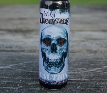 Wicked Nightmare extract bottle beside glass illustrating hot sauce intensity.