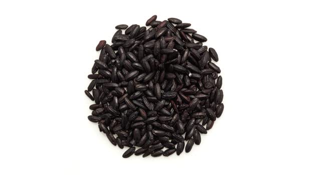 Yupik black rice grains beside fresh vegetables for salads or sides.